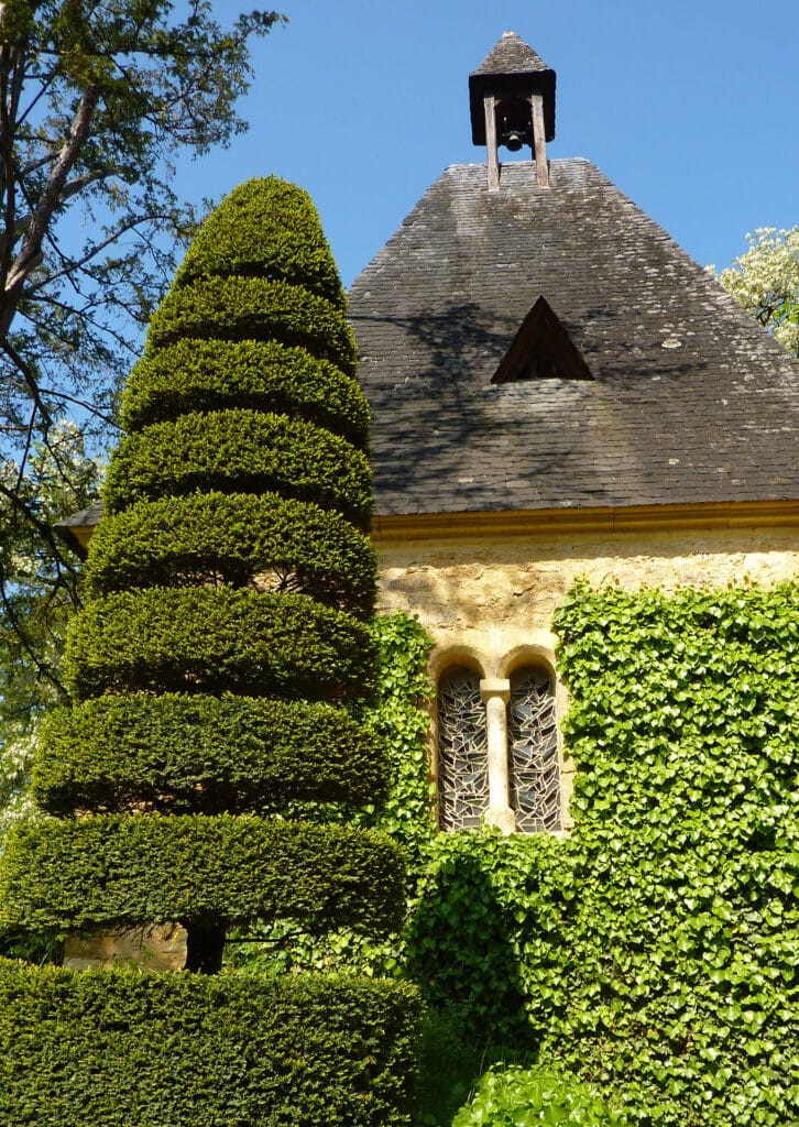 Chapelle ancienne, topiaire sculpté et mur de lierre Chapeau de cloche d'une petite chapelle en pierre avec toit en ardoise, entourée d'un topiaire en gradins et de lierre grimpant.